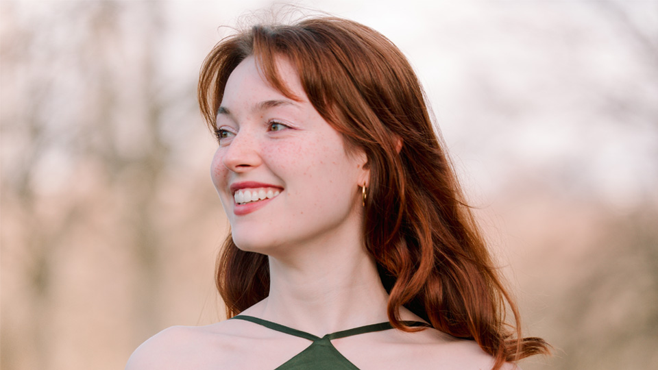 A women with reddish-brown hair, smiling to the side, wearing a green dress.